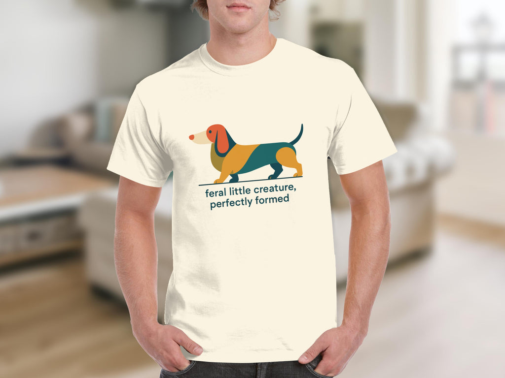 Cream t-shirt with a stylized dachshund graphic and text reading "feral little creature, perfectly formed".