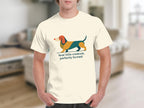 Cream t-shirt with a stylized dachshund graphic and text reading "feral little creature, perfectly formed".
