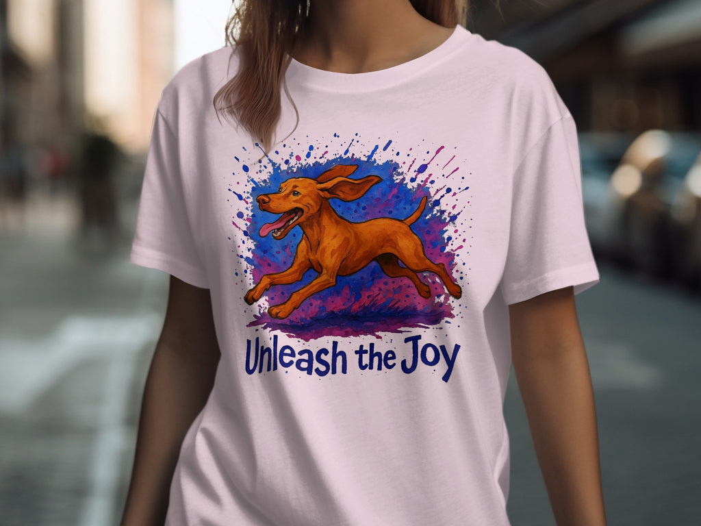 White t-shirt with a brown dog running through a colorful splash design and text reading "Unleash the Joy".