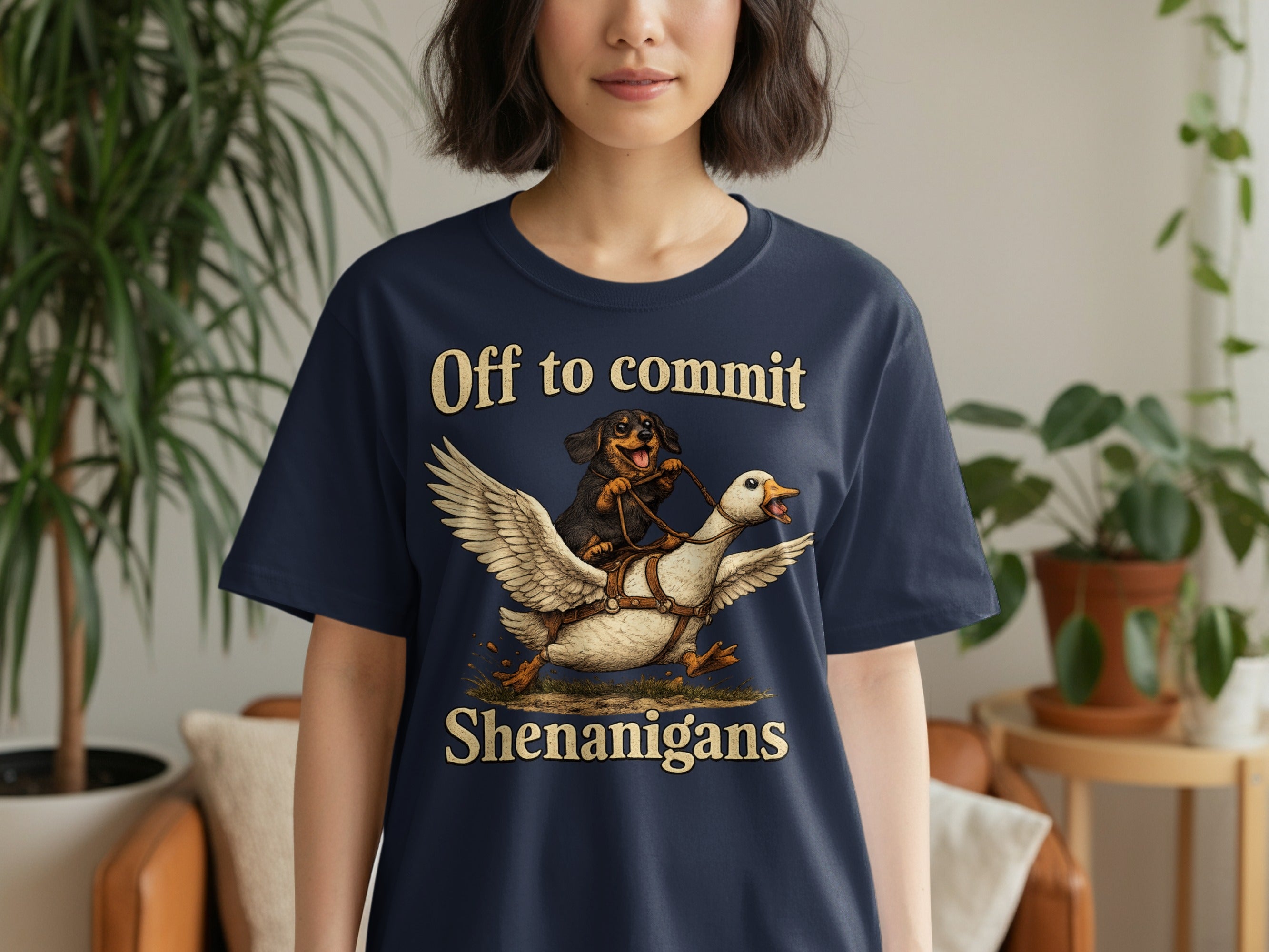 Dark t-shirt with text "Off to commit Shenanigans" above a dog riding a flying goose.