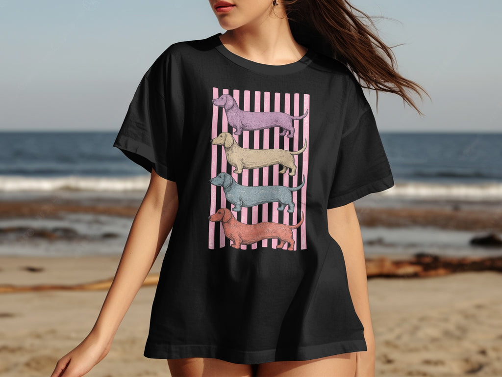 Black t-shirt featuring four stacked, illustrated dachshunds on a pink striped background.