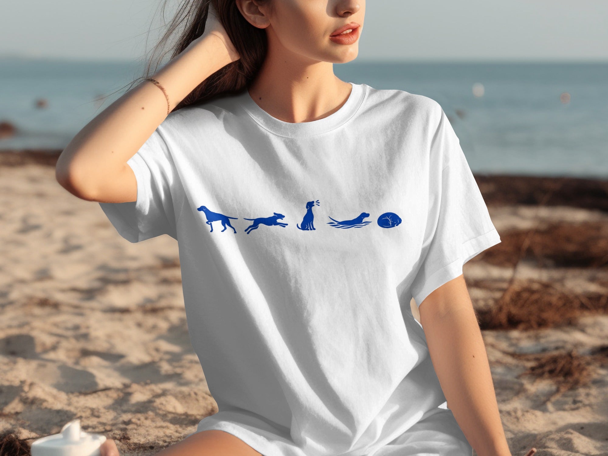 White t-shirt with blue cartoon dogs in various poses on the beach.