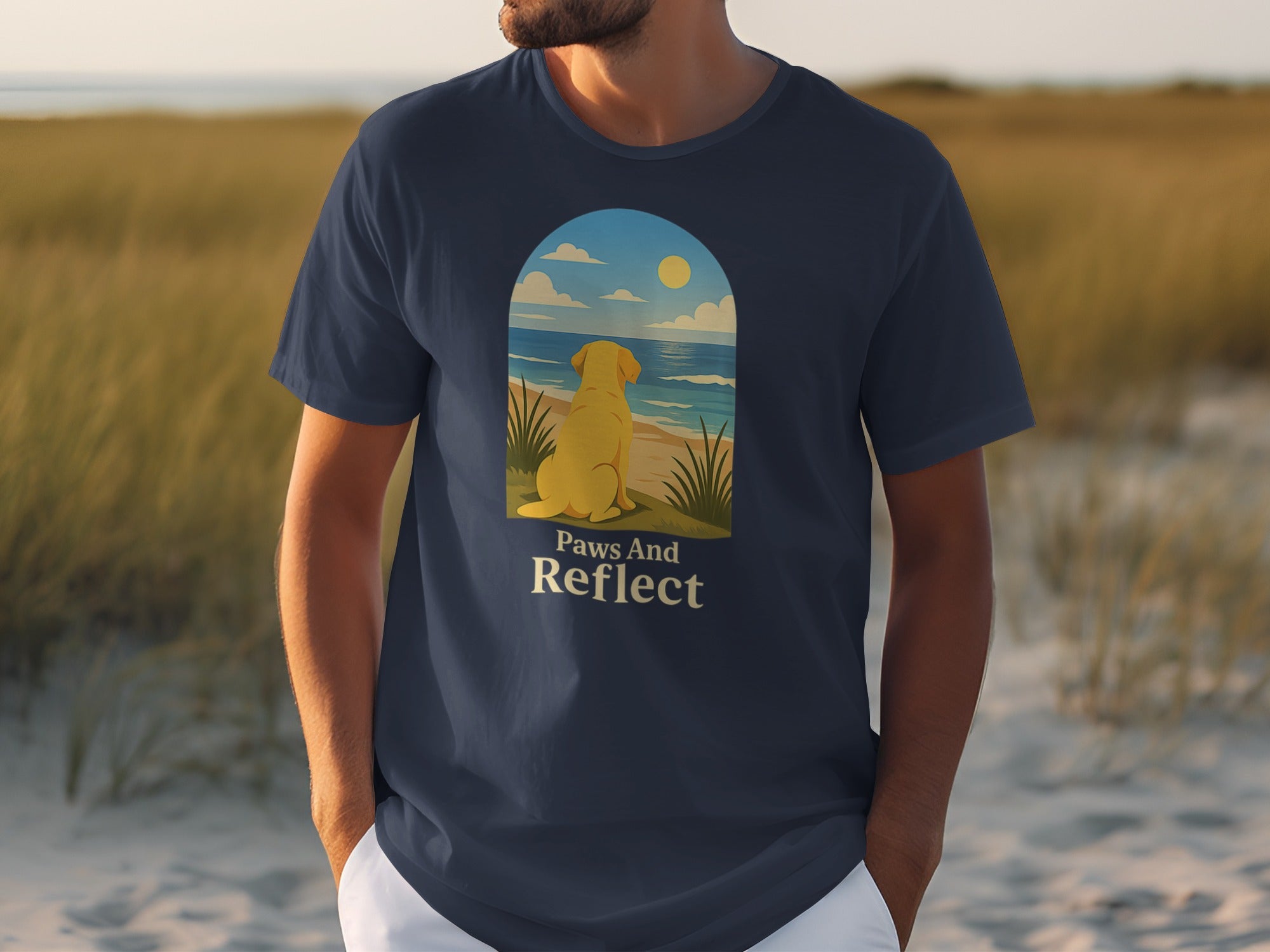 Dark blue t-shirt with a yellow dog looking at the ocean, text reads "Paws And Reflect".