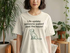 Cream t-shirt with a dog graphic and text "Life update: someone walked past the house!".