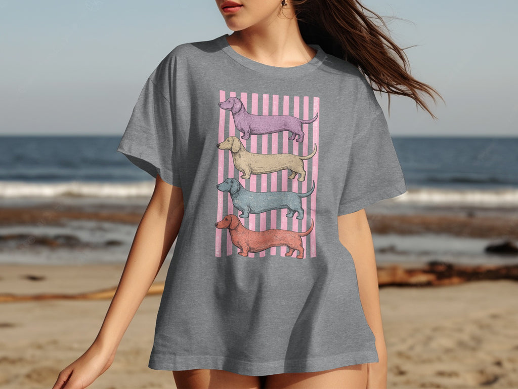 Gray t-shirt with four stacked dachshunds in pastel colors on pink stripes.