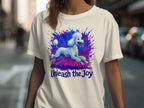 White t-shirt with blue poodle and text "Unleash the Joy" amidst colorful splatters.
