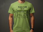 Green t-shirt with black line drawing of a dog in a hat and text "Every walk is an investigation".