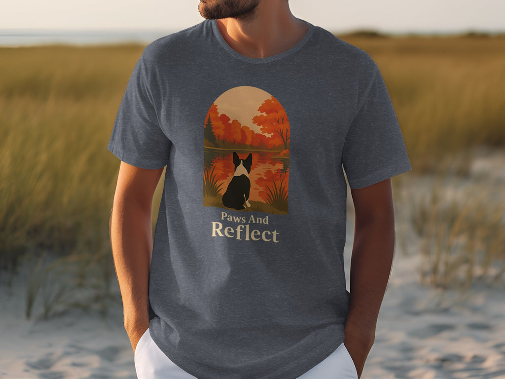 Dark gray t-shirt with illustration of a dog sitting by a lake with fall foliage, text "Paws And Reflect".
