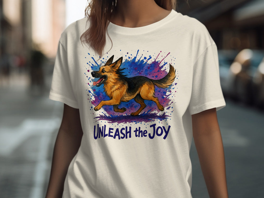 White t-shirt featuring a German Shepherd running amidst a watercolor splash with the text "UNLEASH the Joy".