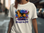 White t-shirt featuring a German Shepherd running amidst a watercolor splash with the text "UNLEASH the Joy".