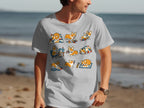 A light grey t-shirt with a graphic of nine cute corgis doing various activities in colorful blocks.