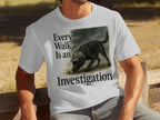 White t-shirt graphic of a black dog wearing a deerstalker hat with text "Every Walk Is an Investigation".