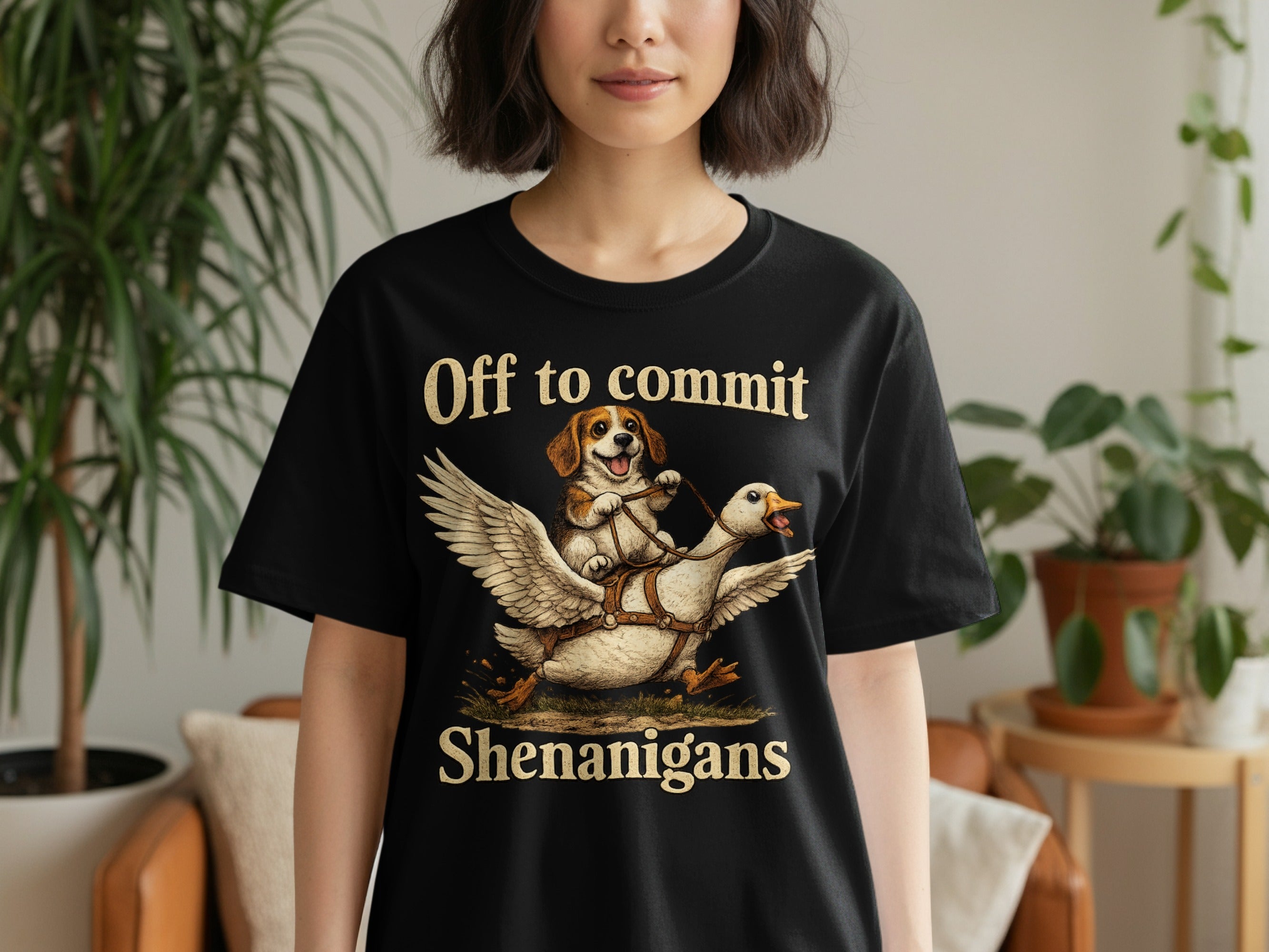 Black t-shirt with dog riding goose and text "Off to commit Shenanigans".