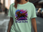Mint green t-shirt with brown dog running through splattered paint, "Unleash the Joy" text.