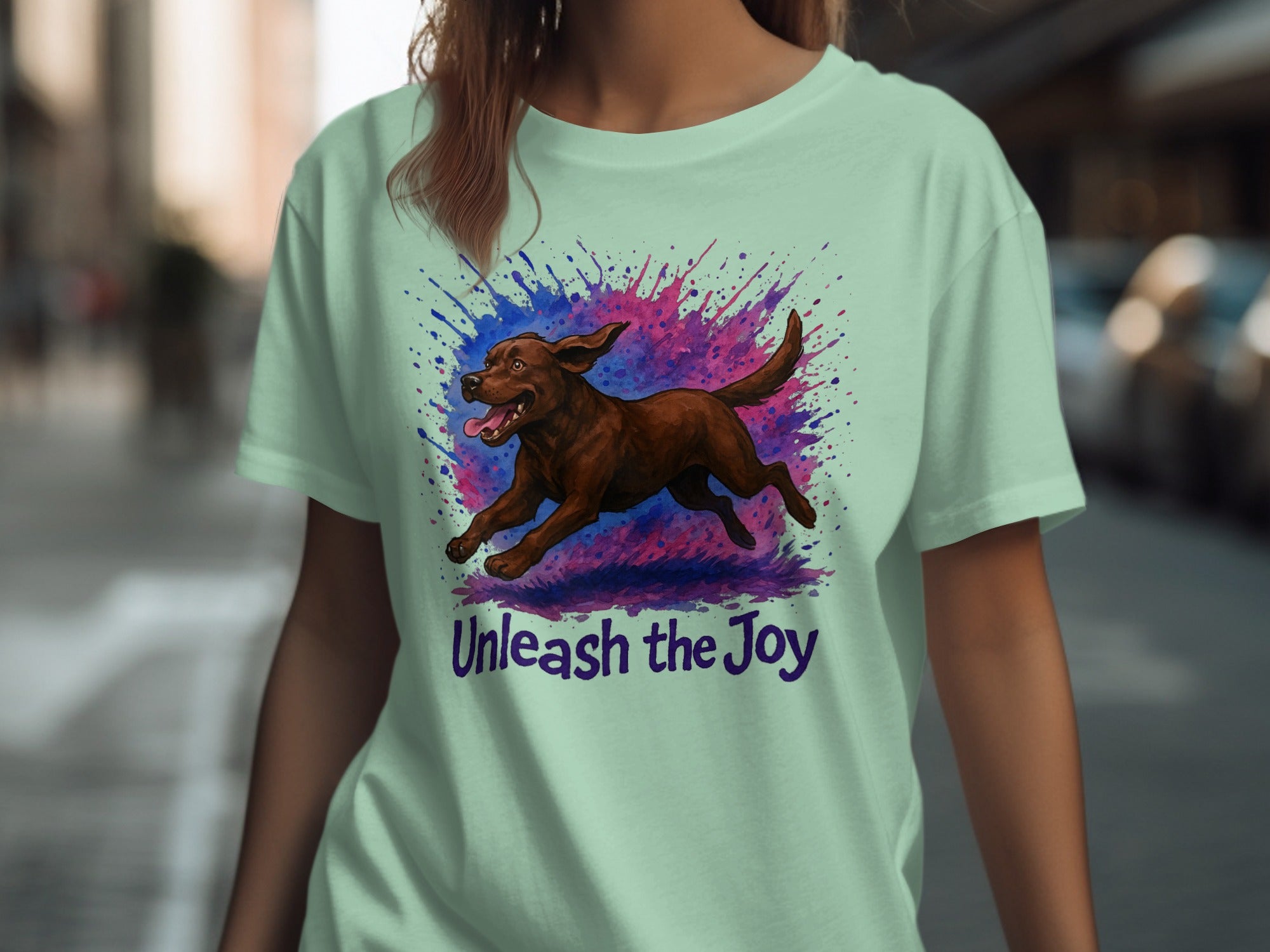 Mint green t-shirt with brown dog running through splattered paint, "Unleash the Joy" text.