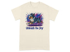 Cream t-shirt with a watercolor Australian Shepherd running through a colorful splash with text "Unleash the Joy".