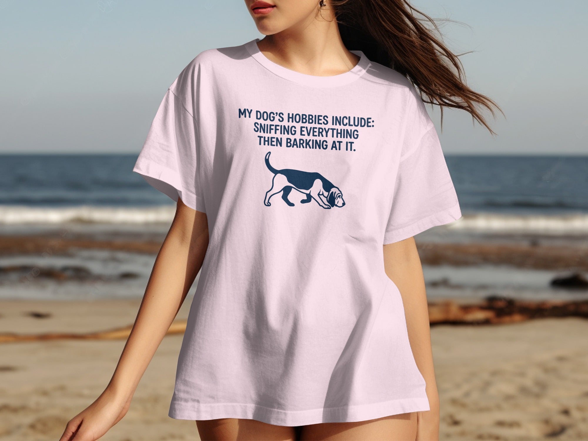Light pink t-shirt with a dog sniffing and text "My dog's hobbies include: sniffing everything then barking at it."