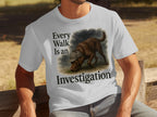 White t-shirt with brown dog wearing a hat, text says "Every Walk Is an Investigation".