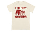 Cream t-shirt with red text "HERD FIRST. EXPLAIN LATER." and a dog graphic.