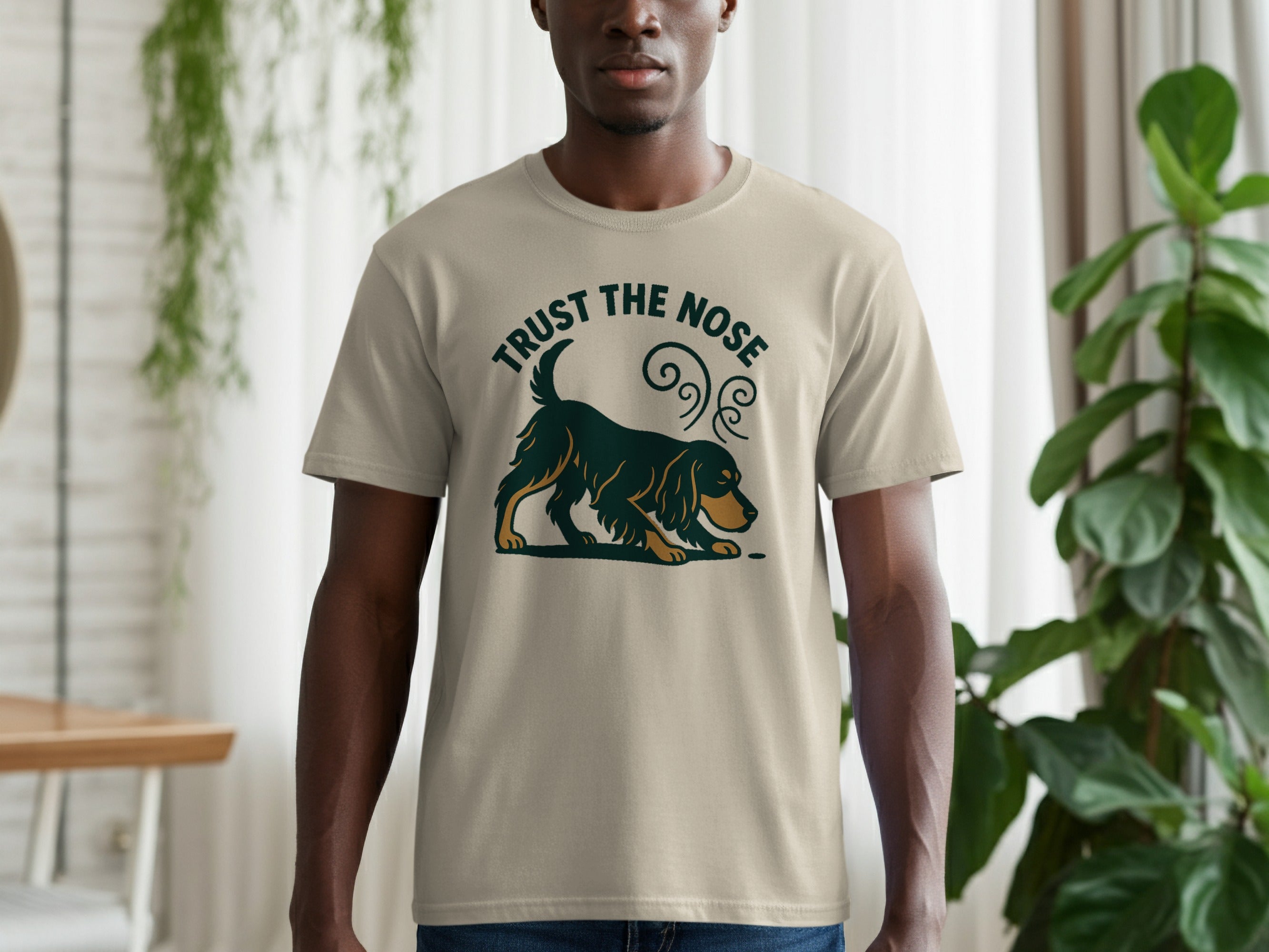 Light tan t-shirt with a dark green and gold dog graphic and "TRUST THE NOSE" text.