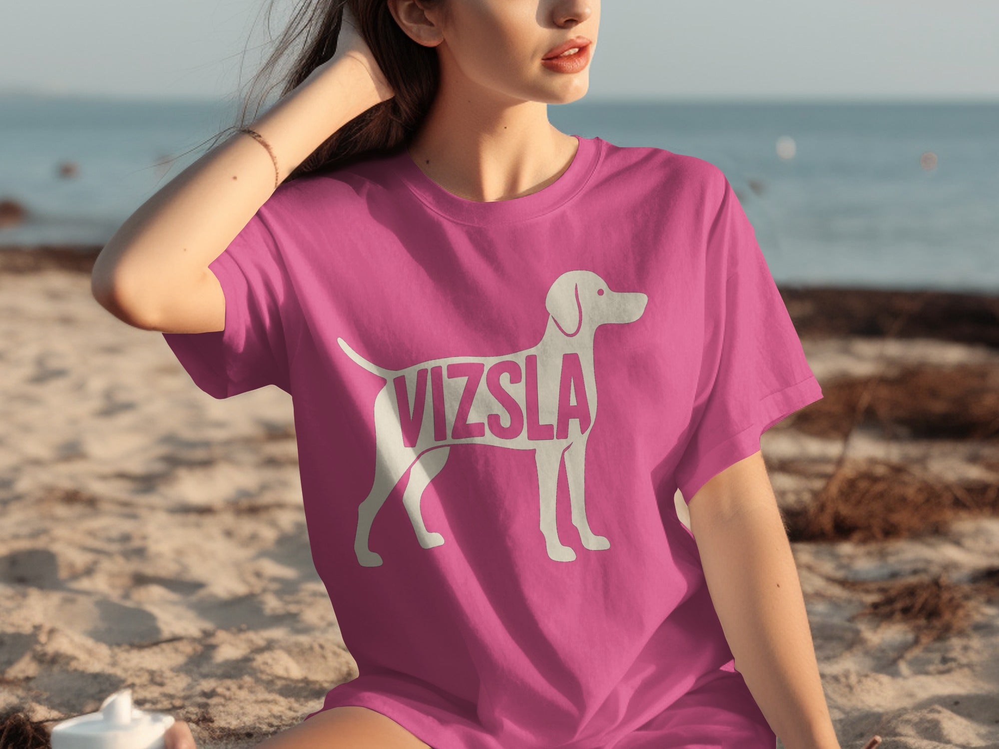 Pink t-shirt with white Vizsla dog silhouette and text on the beach.