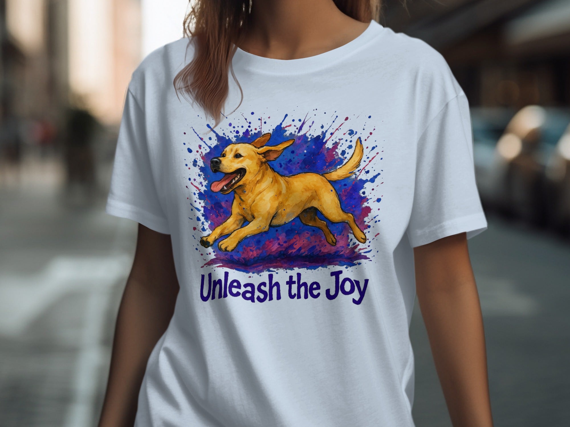 White t-shirt with a yellow dog in mid-stride, surrounded by a colorful splash, and text that reads "Unleash the Joy."