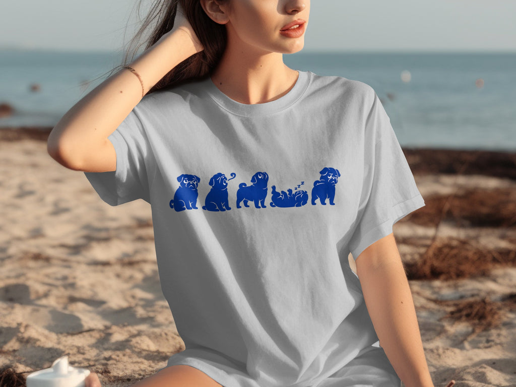 Light blue t-shirt with blue pug illustrations in various poses on a beach.